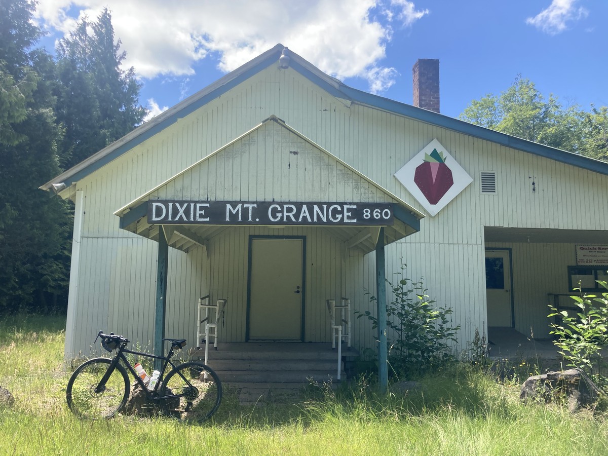 Dixie Mt. Grange Bike leaning against the front of a lightly-used but still maintained country grange hall. Sign reads “Dixie Mt. Grange 860” with a large stylized strawberry