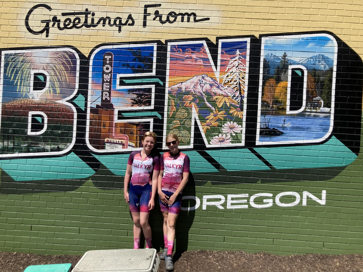 Two VALKYR juniors in front of a mural reading Greetings from BEND Oregon