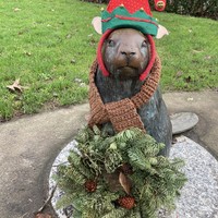 A bronze life-size statue of a beaver, which has been decorated with an elf hat, scarf, and Christmas wreath